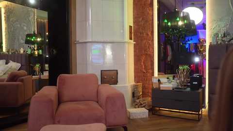 Media: Video of a cozy living room with a plush pink armchair, dark wooden side table, and exposed brick wall, illuminated by green and white pendant lights.