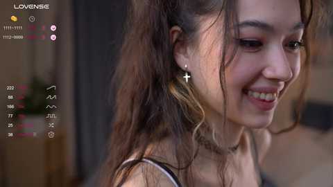 Media: Video of a young Asian woman with long brown hair, smiling, wearing a cross necklace and earrings, in a dimly lit room, with a live stream overlay.