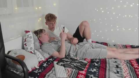 Media: A video of two young boys in pajamas, one reading a book, lying on a bed with a colorful patterned blanket, in a cozy room with fairy lights.