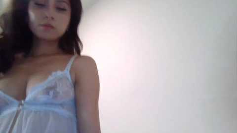 Media: A video of a young Asian woman with long dark hair, wearing a sheer, light blue lace lingerie top that reveals her ample cleavage, against a plain, light-colored background.