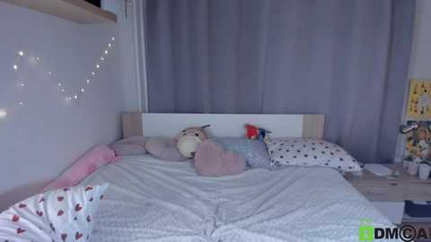 Media: A video of a child's bedroom with a white bed adorned with stuffed toys, a gray curtain, and fairy lights.