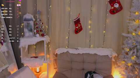 Media: Video of a cozy, Christmas-themed living room with a beige couch, fairy lights, red stockings, snow-covered trees, and a lit lantern.