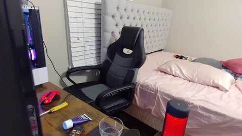 Media: Video of a messy bedroom with a black gaming chair, pink bed, desk cluttered with items, and a window with blinds.