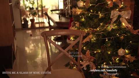 Media: A cozy video of a decorated Christmas tree with white and gold ornaments, illuminated by warm lights, next to a vintage wooden chair in a warmly-lit, elegantly furnished living room.