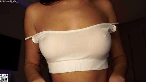 Media: Video of a woman with light brown skin wearing a white, off-the-shoulder crop top that reveals her breasts, with a watermark in the lower left corner.