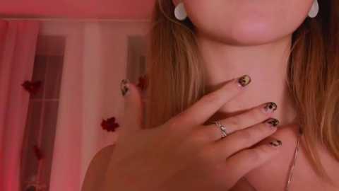 Media: Video of a woman with light skin, wearing a necklace and earrings, her hands adorned with leopard-print manicured nails, in a softly lit room with pink hues and sheer curtains.