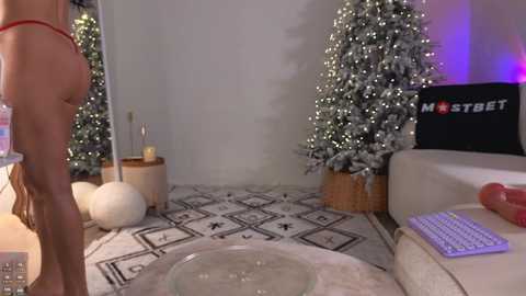 Media: Video of a woman in red lingerie standing in front of a decorated Christmas tree in a minimalist living room with patterned carpet and a white couch.