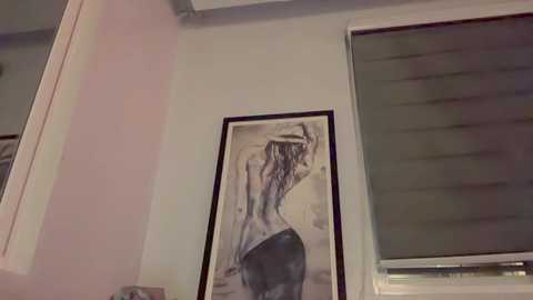 Media: A video of a minimalist room featuring a black-and-white abstract painting of a woman with long hair in a black dress, leaning against a white wall with a window partially covered by blinds.