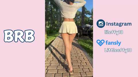 Media: Video of a woman with a slim physique, wearing a white crop top and short beige skirt, walking on a paved path with a tree-lined background. Social media logos, including BBB, Instagram, and FANsy, are displayed on a pink background.