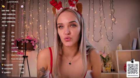 Media: Video of a young woman with light skin, long blonde hair, wearing a red and white Santa hat, and a revealing red top. Background shows Christmas decorations and a phone screen with chat messages.