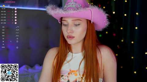 Media: A video of a young woman with long red hair, wearing a pink cowboy hat, white sleeveless top, and a QRCODE. She is indoors with a blurred festive background.