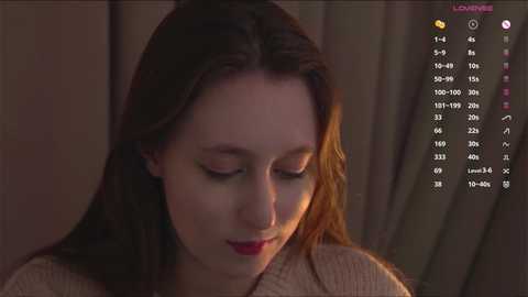 Video of a young woman with fair skin, long brown hair, and closed eyes, wearing a beige sweater. Background features soft, warm lighting and a vertical color gradient chart.