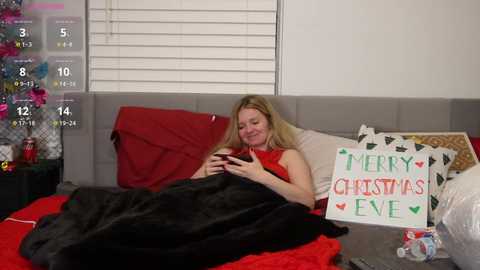 Media: Video of a woman in a red dress, lounging in a bed, holding a mug, surrounded by festive decor.