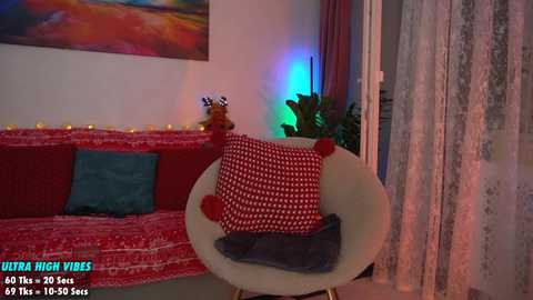 Media: Video of a cozy living room with a red-patterned couch, white chair, colorful cushions, and a large, vibrant painting on the wall.