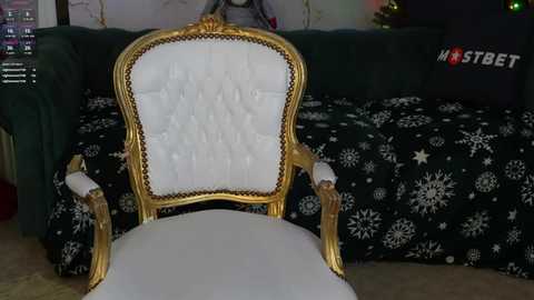 Media: Video of a vintage-style, gold-framed armchair with white, tufted upholstery, positioned in a cozy living room with a dark green couch, a black blanket adorned with white snowflakes, and a Christmas tree in the background.