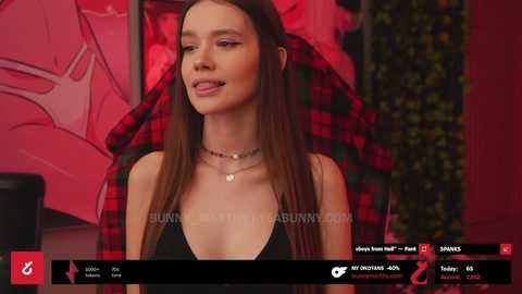 Media: Video of a young woman with long brown hair, wearing a black halter top, standing in front of a pink and red background. She has a slim build and wears a choker necklace.