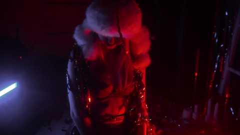 Media: A video of a person dressed in a Santa Claus costume, with red lights illuminating their face and fur-trimmed coat, standing in a dark, industrial setting.