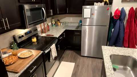 Media: A modern kitchen with dark cabinets, stainless steel appliances, granite countertops, a sink, and hanging red aprons.