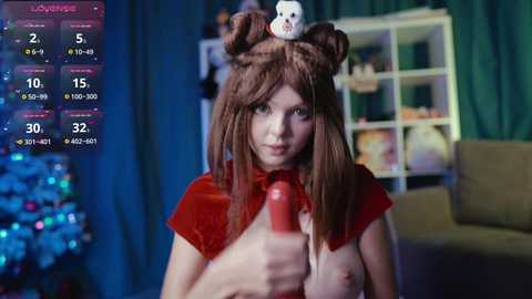 Media: Video of a young woman with fair skin, long brown hair in pigtails, wearing a red cape and white mask, holding a red dildo. Background shows a festive Christmas tree and shelves.