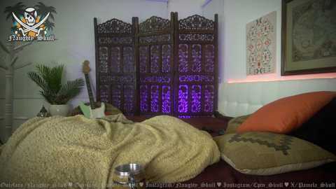 Media: Video of a dimly lit, cozy bedroom featuring a large, intricately carved wooden screen, a beige blanket, a bowl, and a framed artwork on the wall.