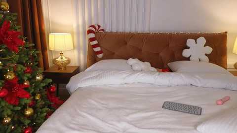 Media: Video of a cozy, festive bedroom with a Christmas tree, brown upholstered headboard, white bedding, and holiday-themed decorations.