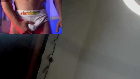 Media: Video of a person in a white Calvin Klein underwear with \"Calvin\" in red, pulling down the waistband. Background shows a dimly lit room with a ceiling light.