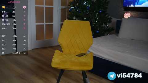 Media: Video of a modern bedroom with a yellow quilted chair, white bed, wooden floor, and a lit Christmas tree in the background.