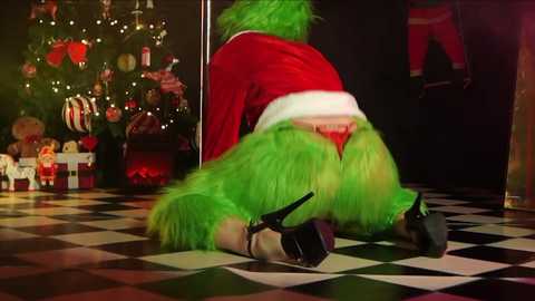 Media: A video of a woman in a Santa costume kneeling on a black-and-white checkered floor, wearing green fur and red lingerie, with Christmas decorations and a teddy bear in the background.