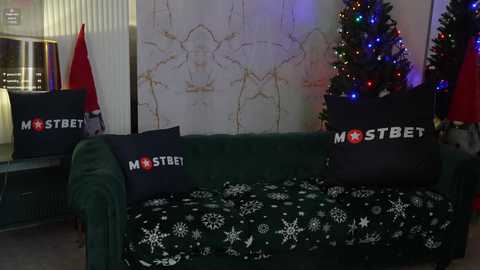 Media: Video of a dark green couch with white snowflake-patterned throw pillows and \"MOSTBET\" text pillows, adorned with a Christmas tree and star decorations.