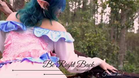 Media: Video of a fair-skinned woman with teal hair in a fantasy costume, featuring a pink corset with blue accents and ruffled sleeves, standing in a lush forest. Text overlays: \"Be Right Back\" and \"Forgive me!\