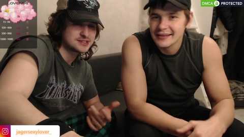 Media: Video of two young men, one with curly hair and the other with short hair, wearing dark t-shirts and caps, seated on a couch, smiling. Background includes a wall with a \"LOVE\" sign and pink flowers.