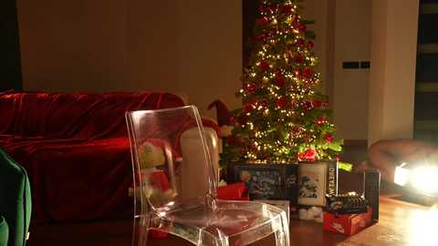 Media: A video of a cozy living room with a transparent chair, a lit Christmas tree, a plush red sofa, and gift-wrapped presents, all bathed in warm, festive lighting.