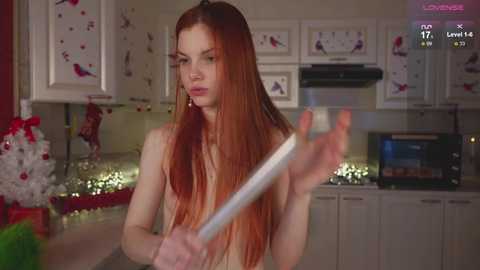 Media: Video of a topless, pale-skinned, red-haired woman holding a knife in a festive kitchen.