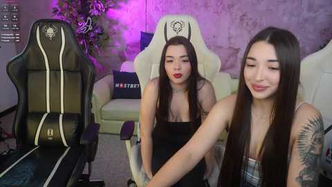 Media: Video of two young women with long dark hair, one with tattoos, sitting on gaming chairs in a dimly lit room with purple lighting and a plant in the background.