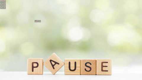 Media: A video of six wooden letter blocks spelling \"PAUSE\" with a soft-focus green background. The blocks have a light brown finish and are arranged horizontally on a white surface. The letters are cut out and filled with black paint, creating a simple, modern aesthetic.