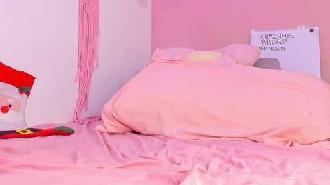 Media: A video of a pink-themed bedroom with a neatly made bed, a Santa Claus pillow, and a \"Christmas Wish Wall\" sign. The room is soft and cozy, exuding a festive atmosphere.