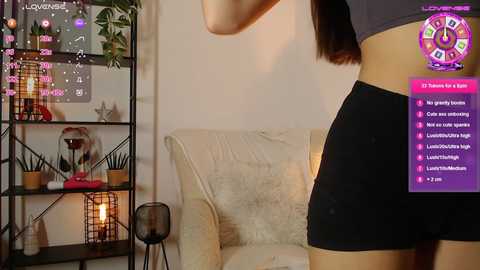 Media: A video of a woman in black shorts standing in a cozy living room with a cream-colored couch, a black metal shelf, and a glowing lantern.