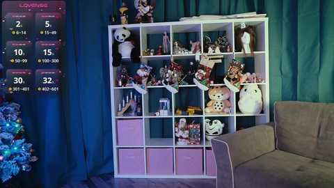 Media: A video of a cozy living room with a white, square-shaped shelving unit filled with plush toys, holiday decorations, and a pink storage bin, against teal curtains. A beige armchair is in the foreground.