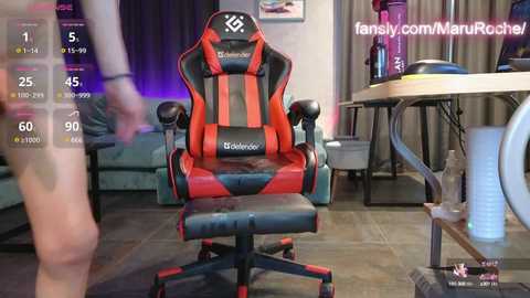 Media: Video of a gamer with fair skin wearing a red and black gaming chair, sitting in a dimly lit room with a desk, water bottle, and a keyboard visible.