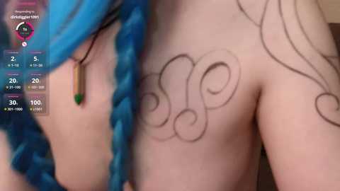 Media: A close-up video of a person with pale skin, blue hair, and intricate black tattoos swirling across their shoulder. The background is blurred, focusing on the intricate designs.