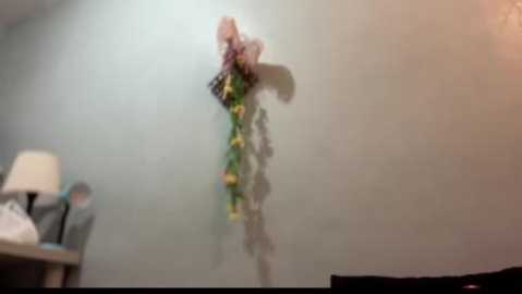 Media: A blurry video of a person in a white shirt and black pants hanging a colorful, floral wreath on a light gray wall in a dimly lit room.