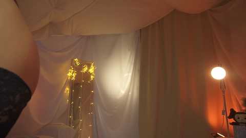 Media: A video of a cozy, dimly lit room with white drapes, a glowing lamp, and a soft, golden glow from fairy lights.