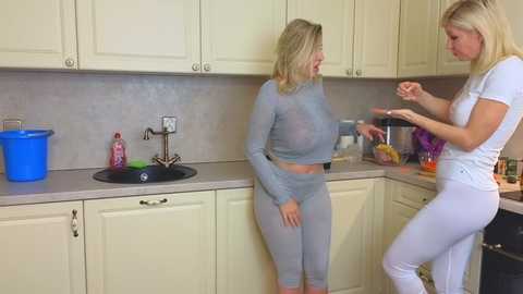 Media: Video of two blonde women in matching grey workout gear in a kitchen; one woman pours coffee, the other laughs.