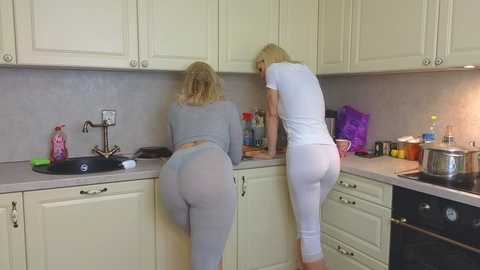 Media: Video of two women with blonde hair, wearing tight grey leggings and crop tops, cleaning a white kitchen with cabinets, sink, and countertop cluttered with dishes.