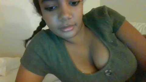 Media: Video of a young South Asian woman with medium skin tone and braided hair, wearing a low-cut green top that reveals cleavage, in a dimly lit room.