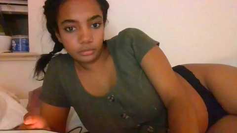 Media: A video of a young woman with dark skin, wearing a green button-up top and black shorts, lying on a bed, her long dark hair tied in pigtails.