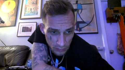 Media: Video of a tattooed man with short brown hair, wearing a black hoodie, in a room with abstract art and a leather couch.