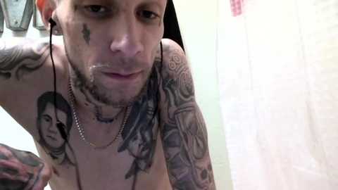 Media: Video of a shirtless, tattooed man with multiple facial piercings and green hair, wearing several chains, in a bathroom with a white shower curtain.