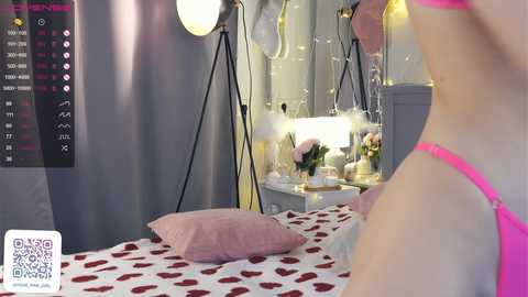 Media: Video of a modern, feminine bedroom with a pink and white polka dot bedspread, a woman in pink lingerie, and a calendar on the wall.