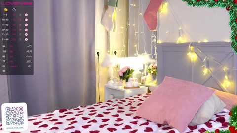 Media: Video of a cozy bedroom with a white bed adorned with red heart-patterned sheets, pink pillows, and festive string lights. The walls are decorated with Christmas-themed ornaments and a calendar showing the date.